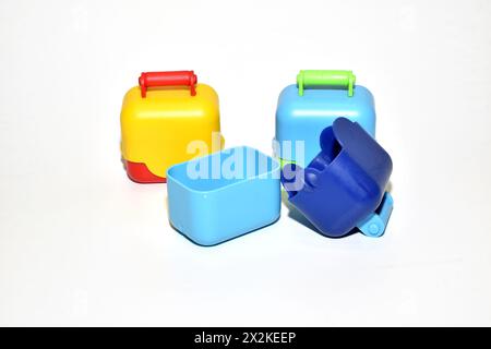 On a white background lie toy chests with handles, made of plastic, painted in various colors. Stock Photo