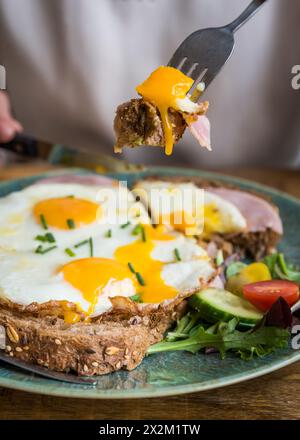 Close up of fried eggs and ham on bread on a plate being eaten on a wooden table in café restaurant Stock Photo