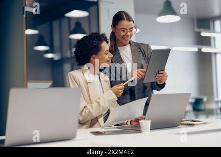 Stylish female executives managers discussing financial accounting papers and using digital tablet  Stock Photo