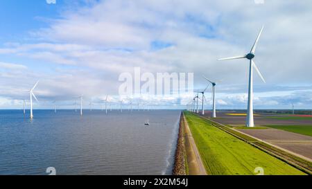 A row of majestic wind turbines stands elegantly next to a calm body of water under the clear Spring sky in the Netherlands. windmill turbines offshore and onshore in the Noordoostpolder Netherlands Stock Photo