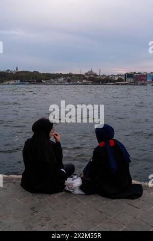 Two veiled women nibble at the edge of the Golden Horn estuary with the great mosque of Saint Sophia, originally a Christian basilica and the most imp Stock Photo