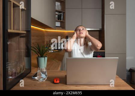 Young woman shouting trying to not to hear the loud noise from neighbor apartment in building while they renovate home and she cant work on laptop or Stock Photo