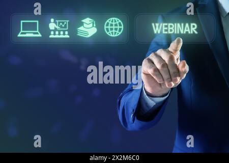 Webinar. Businessman using virtual screen with icons on blue background, closeup Stock Photo