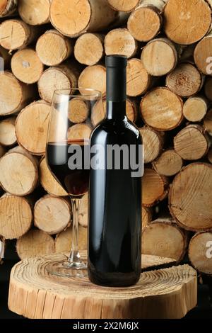 Stylish presentation of red wine in bottle and wineglass near wooden logs Stock Photo