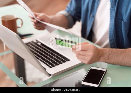 Online bill payment concept. Man using credit card and laptop to paying domestic bills. Close up view of young man hands making online purchase using mobile phone Stock Photo