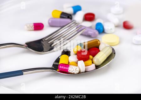 Several mixed medicine pills full on metal spoon on white plate with fork, healthy diet concept. Stock Photo