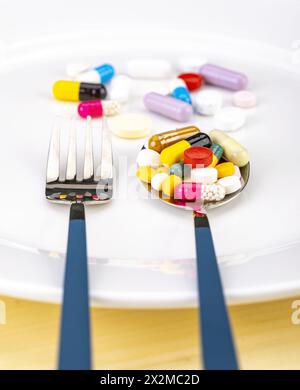 Several mixed medicine pills full on metal spoon on white plate with fork, healthy diet concept. Stock Photo