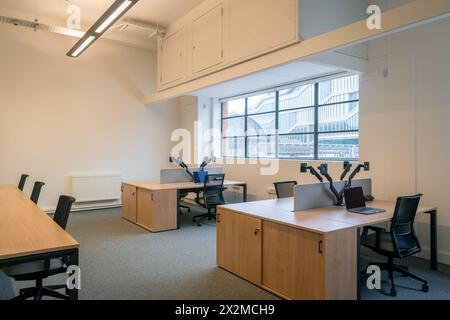 A contemporary office space with wooden desks, chairs, computers, and a large window Stock Photo