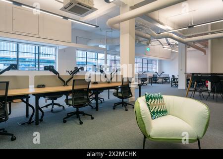 A well-lit contemporary office space featuring a row of desks with ergonomic chairs and computer monitors No people present Stock Photo