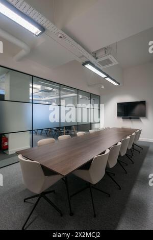 Contemporary conference room featuring a large wooden table, white chairs, flat-screen TV, and glass partitions Stock Photo