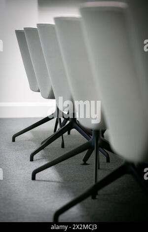 A close-up of contemporary white office chairs lined up neatly on a dark, textured carpet, illustrating a professional and organized office environmen Stock Photo