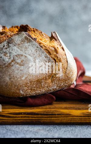 A close-up of a crusty artisan sourdough loaf made with wholesome rye flour, resting on a rustic wooden board with a burgundy cloth Stock Photo