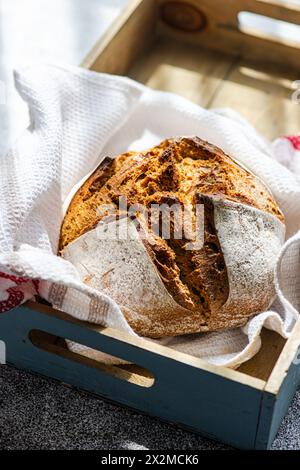 A fresh loaf of artisanal sourdough bread made from rye flour, presented in a wooden tray with a linen cloth, showcasing a rustic kitchen theme Stock Photo