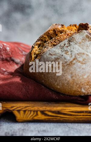 Artisanal sourdough bread made with rye flour, displayed on a wooden cutting board with a red cloth backdrop Stock Photo