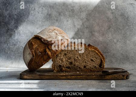 A rustic loaf of rye sourdough bread, freshly baked and sliced on a wooden cutting board, with a knife alongside Stock Photo