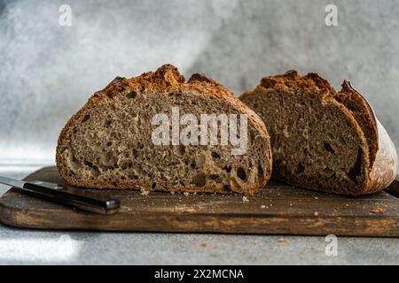 A freshly sliced loaf of homemade rye sourdough bread sits on a rustic wooden cutting board, showcasing its airy texture and crust Stock Photo