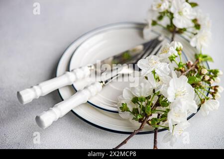 Elegant spring table setting featuring white cherry blossoms on a branch, paired with clean white and blue striped plates and silver cutlery with whit Stock Photo