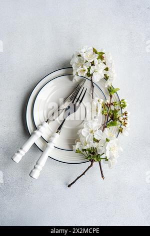 Elegant table setting with white cherry blossoms on a stack of plates with silverware beside Stock Photo