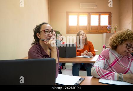 An attentive mature woman participating in a classroom lesson with fellow adult learners engaged in education Stock Photo