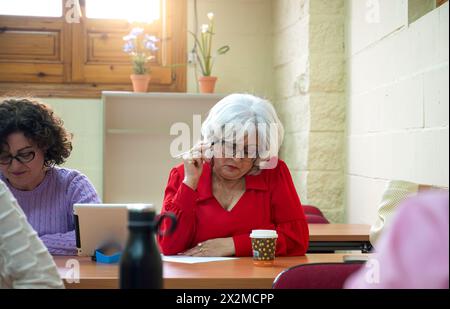 Senior women concentrate on their studies in a classroom setting, showcasing lifelong learning and education Stock Photo