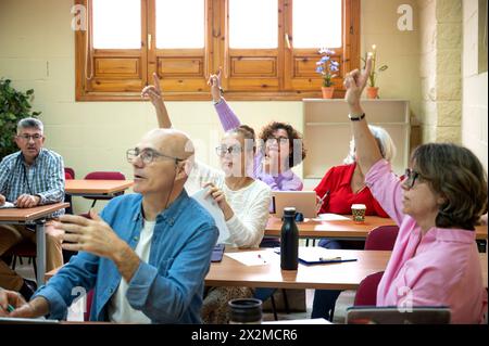 A diverse group of attentive senior students participate enthusiastically in a classroom discussion, with some raising their hands to answer or ask qu Stock Photo