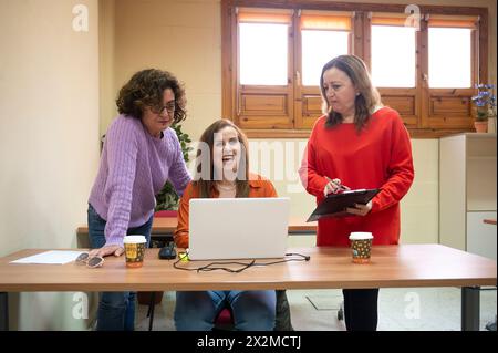 Three enthusiastic professional women collaborate on a project around a laptop in a well-lit office setting Stock Photo