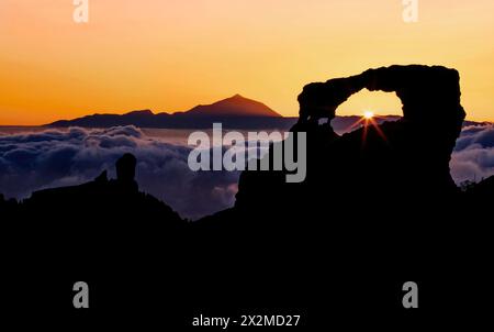 Captivating sunset hues bathe the Roque Nublo and Mount Teide silhouettes, with a sea of clouds floating beneath in Gran Canaria Stock Photo