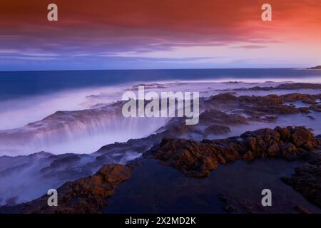The twilight sky casts a calming blue and orange palette over the Bufadero de La Garita, with its frothy waves amidst rocky outcrops in Gran Canaria Stock Photo