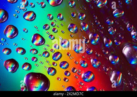 Vibrant raindrops on the surface of a compact disc create a rainbow of reflected colors, showcasing the light diffraction phenomenon. Stock Photo