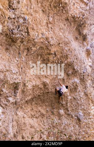 An individual expertly scales a challenging limestone rock wall, displaying determination and athletic ability in a vertical outdoor climb Stock Photo