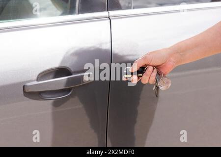 A close-up shot of a hand holding a keyless entry remote to unlock a modern grey car door Stock Photo