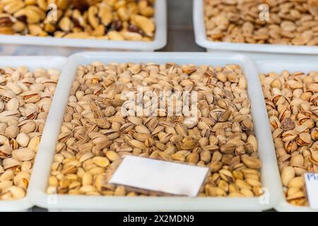 Assorted trays of pistachios on display at a market, with focus on the shelled nuts in the foreground Stock Photo