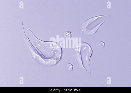 A macro shot capturing the artistic swirls and droplets of transparent gel on a purple-toned smooth background Stock Photo