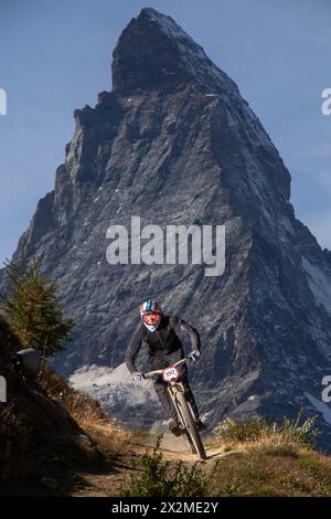 Mountain biker descends a trail with the jagged peak of Matterhorn in the backdrop during a summer adventure Stock Photo