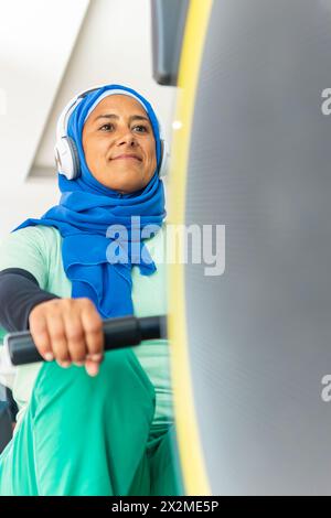 A focused woman in hijab works on her laptop at a home desk with books ...