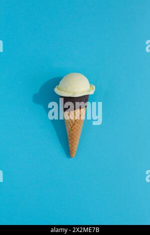 A vibrant cream ice cream scoop sits atop a classic waffle cone against a blue background, casting a playful shadow Stock Photo
