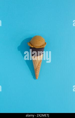 A vibrant coffee ice cream scoop sits atop a classic waffle cone against a blue background, casting a playful shadow Stock Photo