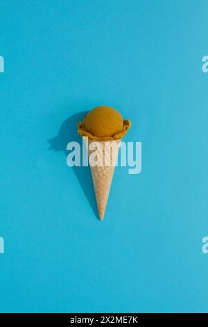 A vibrant Pistachio ice cream scoop sits atop a classic waffle cone against a blue background, casting a playful shadow Stock Photo