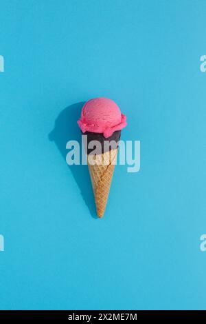 A vibrant Strawberry ice cream scoop sits atop a classic waffle cone against a blue background, casting a playful shadow Stock Photo