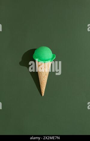 A vibrant green ice cream scoop sits atop a classic waffle cone against a green background, casting a playful shadow Stock Photo