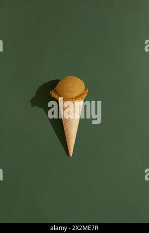 A vibrant coffee ice cream scoop sits atop a classic waffle cone against a green background, casting a playful shadow Stock Photo