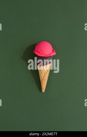 A vibrant Strawberry ice cream scoop sits atop a classic waffle cone against a green background, casting a playful shadow Stock Photo