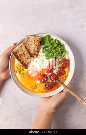 A savory plate of Turkish eggs perched on creamy Greek yogurt, drizzled with spiced butter and garnished with tomatoes and parsley, served with toast Stock Photo
