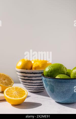 Bowls of vibrant yellow lemons and green limes presented on a light surface, with a half-cut lemon in the foreground Stock Photo