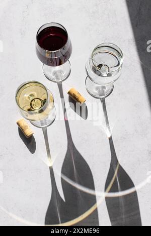 Three wine glasses filled with red, white, and no wine cast long shadows on a textured surface, showcasing a minimalistic and elegant design. Stock Photo