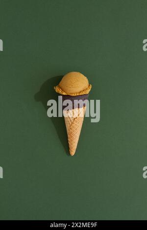 A vibrant pistachio ice cream scoop sits atop a classic waffle cone against a green background, casting a playful shadow Stock Photo