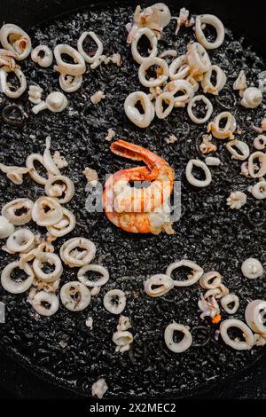 Top view of traditional black rice paella cooked with squid ink, baby squid, and shrimp, showcasing the Valencian style with a perfect socarrat. Stock Photo