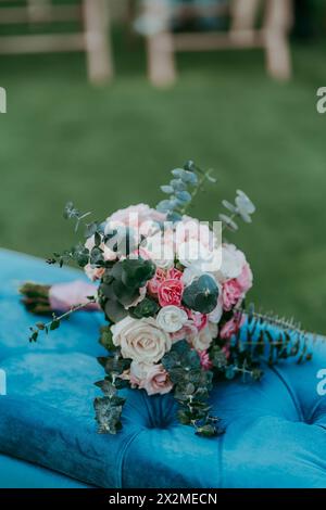 Elegant bridal bouquet with a mix of roses and greenery, placed on a blue velvet chair Stock Photo