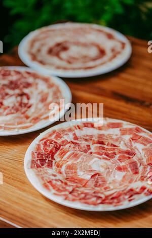 Freshly sliced Iberian Ham arranged on plates for cooking, displayed on a wooden table Stock Photo