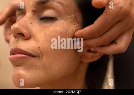 Latina man receiving an ayurvedic massage on the face with specific pressure points Stock Photo